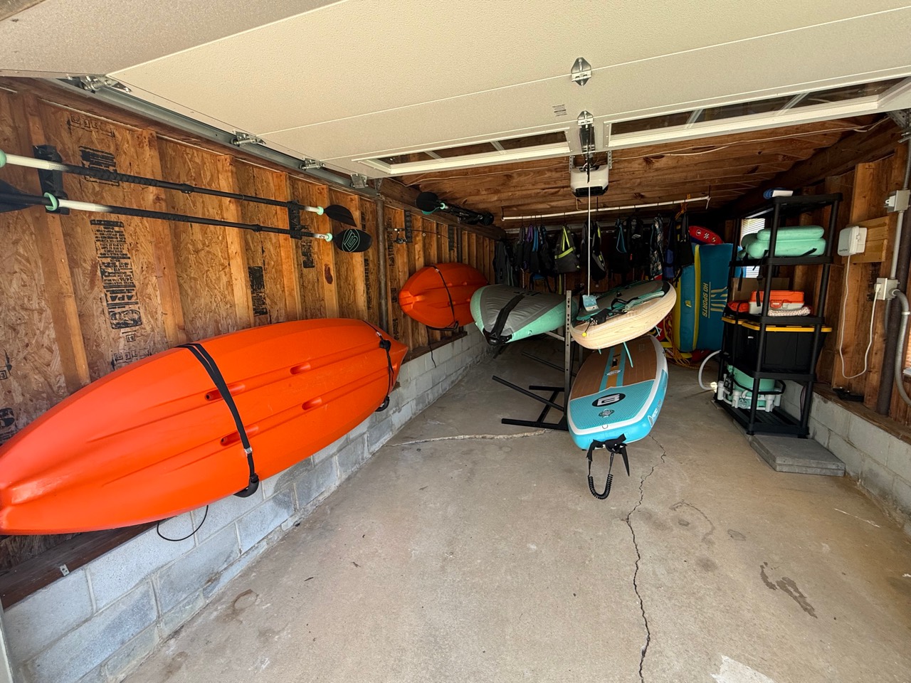 Boat house stocked with kayaks, paddle boards, life jackets, and towable floats.
